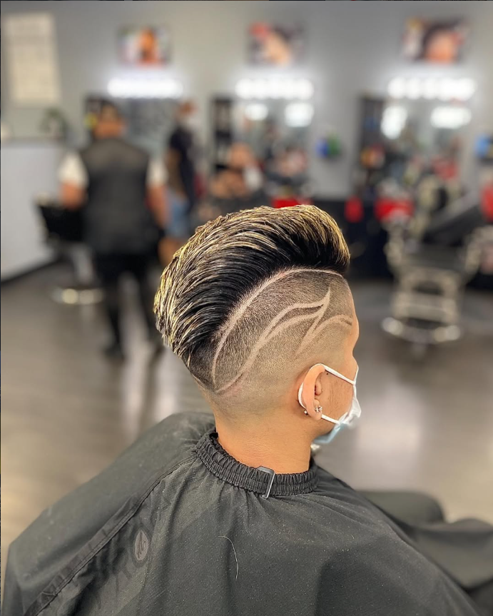 Back-and-side view of a swept-back cut with blonde tips and carved flame designs on the fade